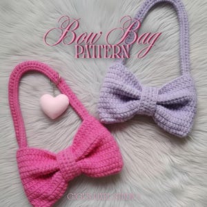 May include: Two crocheted bow-shaped bags, one pink and one lavender, with matching handles. The pink bag has a small heart charm attached. The text "Bow Bag PATTERN" is displayed above the bags. The bags are on a fluffy, light grey surface.