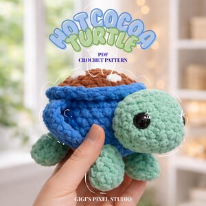 Peut inclure: Une tortue au crochet bleue et verte, portant une tasse de chocolat chaud marron avec des guimauves blanches. Le texte "Hot Cocoa Turtle" et "PDF Crochet Pattern" est visible. Un adorable jouet fait main.