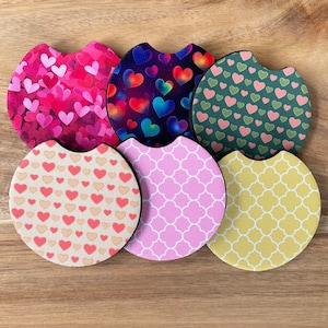 May include: Six round beverage coasters with different patterns. The coasters feature various heart designs, geometric patterns, and a colourful abstract design. The coasters are made of a soft, absorbent material.