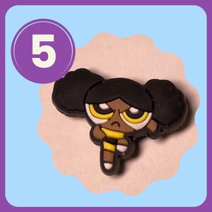 May include: A black and yellow cartoon character with brown skin and angry eyes. The character has black hair with two pigtails and is wearing a yellow and black outfit.