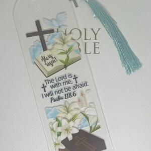 May include: A clear acrylic bookmark with a white dove, lilies, and a cross. The bookmark has a blue tassel and the text "She is risen! The Lord is with me, I will not be afraid. Psalm 118:6"