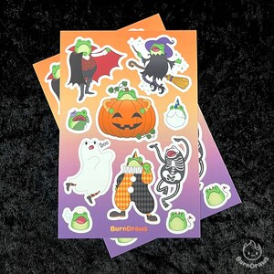May include: A set of 10 Halloween themed frog stickers. The stickers feature frogs dressed as a vampire, witch, ghost, skeleton, clown, and pumpkin. The stickers are printed on white paper with a glossy finish.
