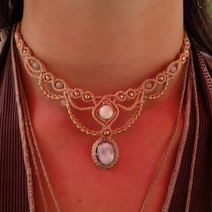 Op de afbeelding: Een delicate macramé choker ketting met een licht roze en witte edelsteen hanger. De ketting is gemaakt van beige koord en heeft gouden kralen.