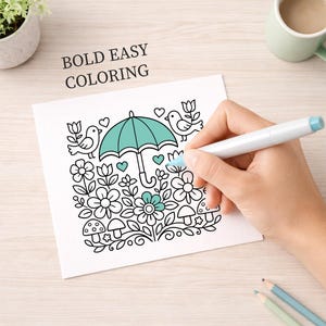 May include: A coloring page with a floral and bird design, featuring an umbrella in the center. The words "BOLD EASY COLORING" are printed at the top. A hand is coloring the image with a blue marker. Two pencils are at the bottom.
