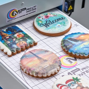 Peut inclure: Plusieurs biscuits décorés avec des motifs imprimés, dont une scène d'Halloween, un paysage et la Tour Eiffel. Un biscuit porte le mot "Welcome". Les biscuits sont sur une surface blanche avec un quadrillage.