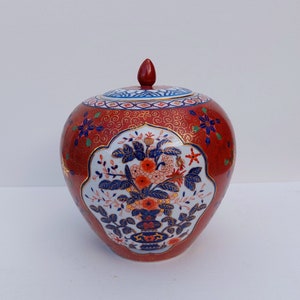 May include: A red and white ceramic jar with a lid. The jar is decorated with blue and gold floral designs. The lid has a red knob.