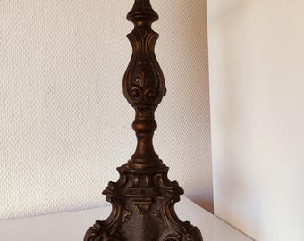 May include: Ornate bronze-colored candlestick holder with a detailed, decorative design. The candlestick features a wide, round top, a slender, sculpted stem, and a three-footed base. The overall height is approximately 12 inches.