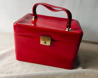 Puede incluir: Un neceser rojo brillante con un asa a juego y un cierre dorado. La caja rectangular tiene un acabado brillante y un asa curvada. Ideal para guardar cosméticos y productos de belleza.