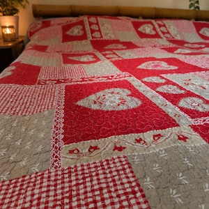 Peut inclure: Une courtepointe patchwork rouge et beige. Elle présente divers motifs, notamment des cœurs, du vichy et des motifs floraux. La couverture de lit est en tissu matelassé, idéale pour le lit.