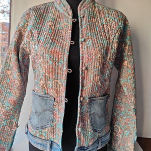 Peut inclure: Une veste à motif turquoise et rose avec une bordure en jean et une fermeture à boutons. La veste a une texture matelassée et un motif paisley.