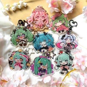 Può includere: Una collezione di portachiavi in acrilico in stile anime con personaggi chibi colorati con grandi occhi e abiti dettagliati. Ogni portachiavi ha un anello di metallo per l'attacco. I personaggi hanno vari colori di capelli, tra cui rosa, verde e blu.