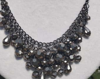 May include: A black chain necklace with a cluster of teardrop-shaped beads. The beads are faceted and have a metallic finish.