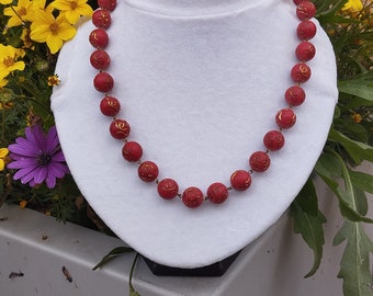 May include: A red beaded necklace with gold accents. The beads are round and have a textured surface. The necklace is displayed on a white mannequin.
