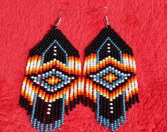 May include: A pair of long, beaded earrings with a geometric pattern in black, white, orange, and blue. The earrings are hanging from silver hooks.