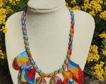 May include: A colourful beaded necklace with a multi-coloured design. The necklace is made of small beads and has a long, flowing design. The necklace is displayed on a white mannequin.