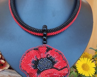 May include: A beaded necklace with a black and red design. The necklace features a pendant in the shape of a red poppy with a black centre. The pendant is accented with a red crystal.