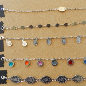 Puede incluir: Cinco pulseras de cadena plateadas con diferentes dijes. Los dijes incluyen peque&ntilde;os c&iacute;rculos plateados, medallones ovalados con un dise&ntilde;o de cruz y piedras de vidrio de colores.
