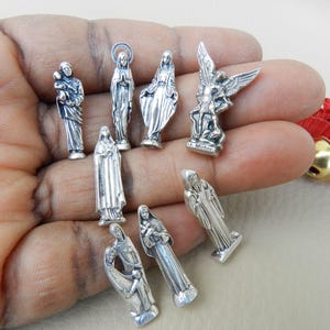 Peut inclure: Une collection de neuf figurines religieuses argentées, dont une représentation d'un ange, une mère et son enfant, et plusieurs figures de saints. Les figurines sont petites et détaillées, et elles constitueraient un bel ajout à toute collection religieuse.