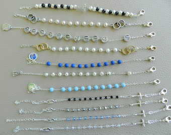 Puede incluir: Diez pulseras de cadena plateada con diferentes dijes y cuentas. Las pulseras presentan cuentas de diferentes colores, incluyendo blanco, azul, negro y transparente. Algunas pulseras tienen dijes, como cruces, anillos y medallones.