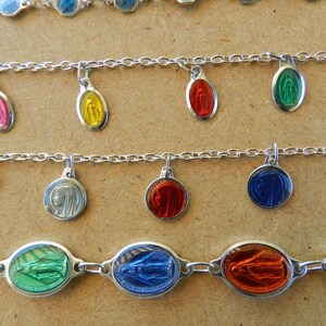 Puede incluir: Tres pulseras de cadena de plata con dijes ovalados y redondos que muestran im&aacute;genes de la Virgen Mar&iacute;a. Los dijes son de varios colores, incluyendo rosa, amarillo, verde, azul, rojo y morado.
