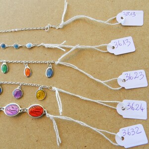 Puede incluir: Cinco pulseras de cadena plateada con abalorios de esmalte de colores. Las pulseras cuelgan de etiquetas blancas con n&uacute;meros escritos a mano: 3513, 3613, 3623, 3624 y 3632.