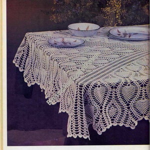 Puede incluir: Un mantel de crochet blanco con un patrón delicado. El mantel está puesto sobre una mesa con platos y cuencos encima. El texto "CROCHET A BEAUTIFUL HEIRLOOM TABLECLOTH" está impreso debajo de la imagen.