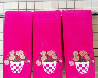 May include: Three pink hand towels with embroidered floral designs. Each towel features a bouquet of flowers in a checkered pot.