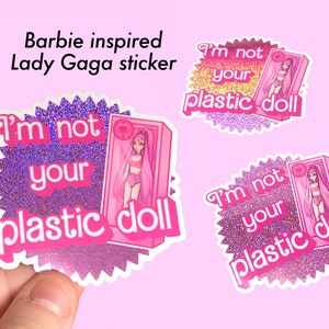 May include: A pink and purple glitter sticker with the text "I'm not your plastic doll" and a cartoon image of a doll in a pink box.