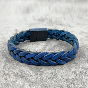 Puede incluir: Un brazalete trenzado de cuero azul con cierre magnético negro.