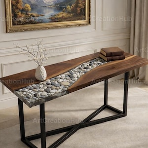 May include: A rectangular wooden table with a river of stones embedded in clear resin. The table has a dark wood finish and black metal legs. A vase with white branches and two books are on the table.