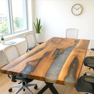 Könnte beinhalten: Ein großer, rechteckiger Holztisch mit einem flussartigen Design. Der Tisch hat eine hellbraune Holzmaserung mit einem grauen Epoxidharz-Mittelteil. Der Tisch ist von schwarzen Bürostühlen umgeben.