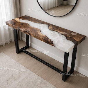 May include: A long, rectangular wooden console table with a white resin river design. The wood has a natural grain pattern, and the table is supported by black metal legs. A round black mirror hangs on the wall above the table.