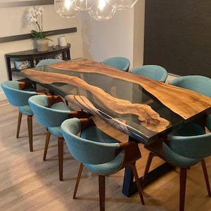 Könnte beinhalten: Ein großer Esstisch aus Holz mit einem durchgehenden Fluss aus klarem Epoxidharz. Der Tisch ist von tealblauen Stühlen mit Holzbeinen umgeben.