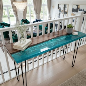 Könnte beinhalten: Eine moderne Konsolentisch mit einer rohen Walnussplatte und einem türkisfarbenen Epoxidharzfluss. Der Tisch hat schwarze Haarnadelbeine und ist etwa 122 cm lang. Der Tisch befindet sich in einem hellen Raum.