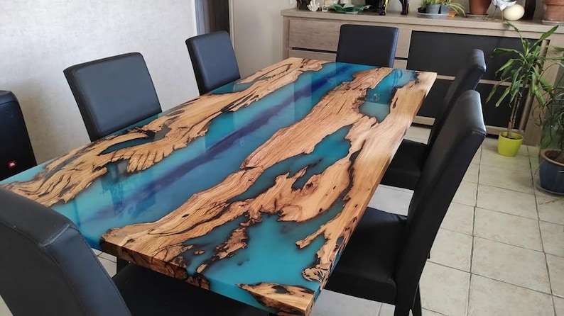 May include: A large wooden dining table with a blue and green epoxy resin inlay. The table is surrounded by black chairs.