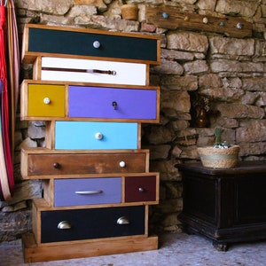 Puede incluir: Una cómoda colorida con cajones en varios tonos de azul, morado, amarillo y verde. La cómoda está hecha de madera y tiene un estilo rústico y de granja.