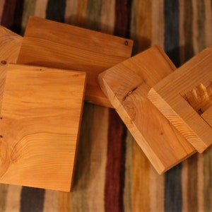 Könnte beinhalten: Fünf Stücke unbehandeltes Holz, jedes mit einer anderen Form und Größe, sind auf einem gestreiften Teppich angeordnet. Das Holz ist hellbraun und hat eine natürliche Maserung.