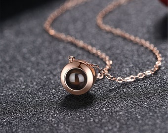 May include: A rose gold necklace with a small round pendant. The pendant has a dark, reflective surface.