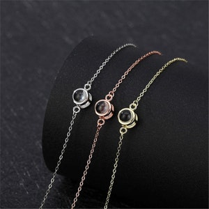 May include: Three silver, rose gold, and gold bracelets with a small round pendant that projects an image when viewed through a small hole.