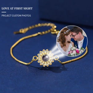 May include: Gold-coloured bracelet with a sunflower pendant and a central projection lens. The pendant is surrounded by small, clear crystals. The bracelet is on a dark blue surface. Text reads: LOVE AT FIRST SIGHT, PROJECT CUSTOM PHOTOS.