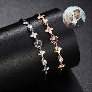 Könnte beinhalten: Zwei silberne und roségoldene Armbänder mit einem kleinen runden Stein in der Mitte jedes Armbands. Die Steine sind von kleinen klaren Steinen umgeben. Die Armbänder bestehen aus einer Kette mit kleinen Blumenanhängern.