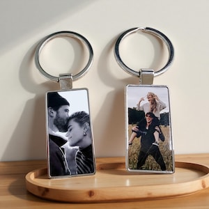 Peut inclure: Deux porte-clés rectangulaires en métal avec des anneaux brisés argentés. Le porte-clés de gauche présente un portrait en noir et blanc d'un couple qui s'enlace. Celui de droite montre une photo couleur d'une personne portant quelqu'un.