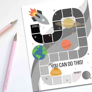 Puede incluir: Un juego de mesa impreso con temática espacial con un cohete, planetas y el texto "YOU CAN DO THIS!". Dos bolígrafos rosas con puntas plateadas están a la izquierda. Un bolígrafo tiene el texto "IS IT FRIDAY YET?"