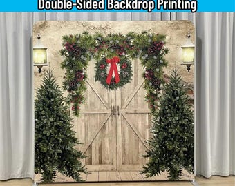 May include: A rectangular backdrop display featuring a printed image of rustic wooden doors flanked by two green Christmas trees. A festive garland with red berries and a central wreath with a red bow hangs above the doors. Text reads: FRAME+CUSTOM FABRIC COVER INCLUDED Double-Sided Backdrop Printing.