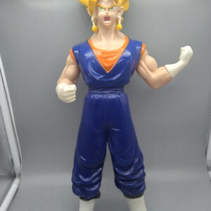 May include: A plastic action figure of a character with spiky yellow hair, wearing a blue and orange sleeveless tunic, blue pants, white gloves, and white boots with yellow tips. The figure has yellow earrings and a determined facial expression.