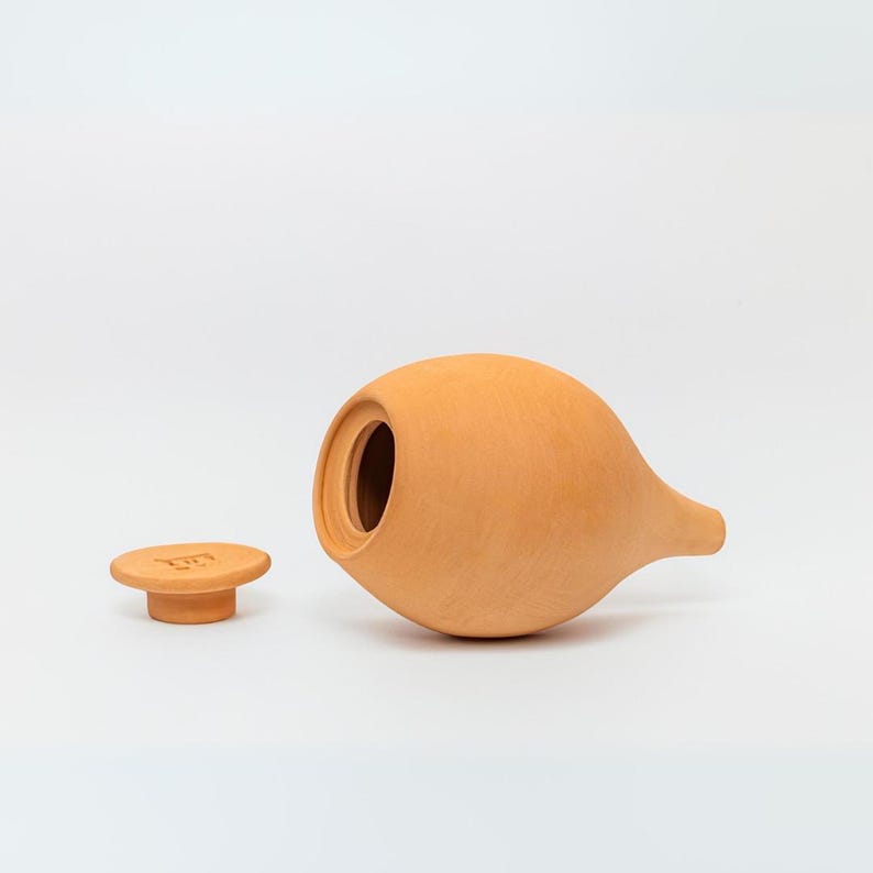 May include: A terracotta ceramic jar with a lid. The jar is a light orange color and has a rounded body with a long, thin spout. The lid is a small, round disc with a raised rim.