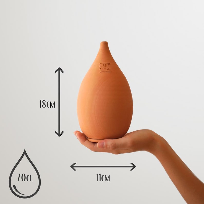 May include: A terracotta-colored, teardrop-shaped ceramic bottle, 18 cm tall and 11 cm wide, is held in a hand. The bottle has the text "LUT OYA" on it. The image also shows a 70cl water drop icon.