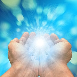 May include: Two hands cupped together with a bright white light shining from within, against a blue and white blurred background.