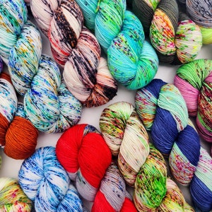 Peut inclure: Une collection de pelotes de laine colorées avec des motifs mouchetés. La laine est disposée en cercle, chaque pelote se chevauchant. Les couleurs incluent le bleu, le vert, le rouge, l'orange, le blanc et le noir.