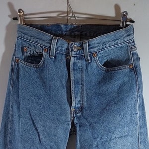 May include: A pair of light blue denim jeans hanging on a hanger. The jeans have a classic five-pocket style and a straight leg.